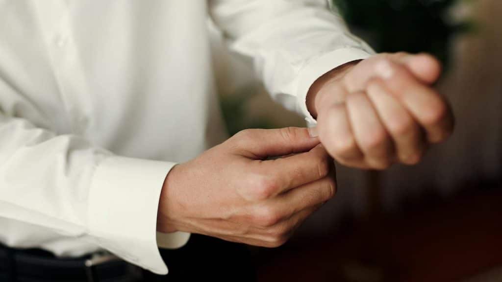 A man fastening the cuff of his white dress shirt.
