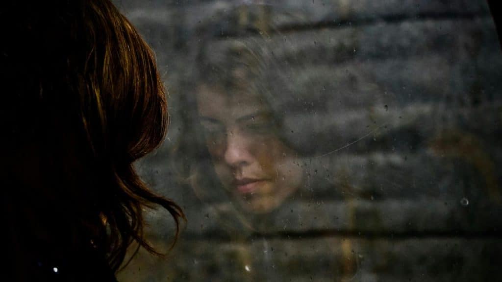 A woman’s face reflected in a foggy, dimly lit window.