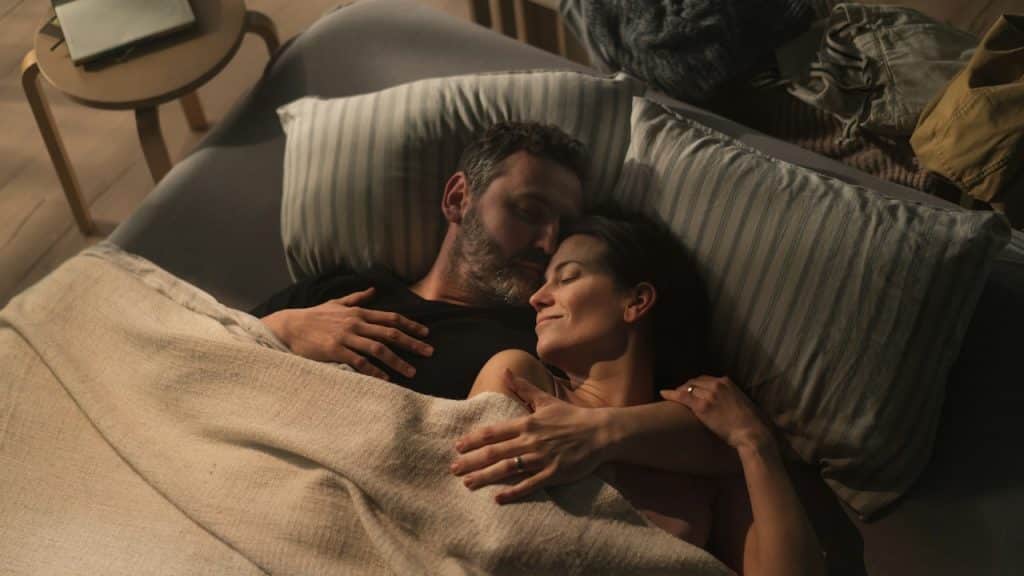 Couple lying awake and embracing in bed under a blanket.