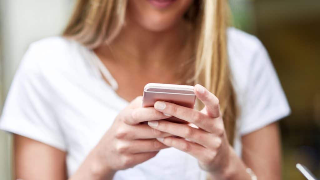 Close-up of a blonde woman texting on a rose gold smartphone.