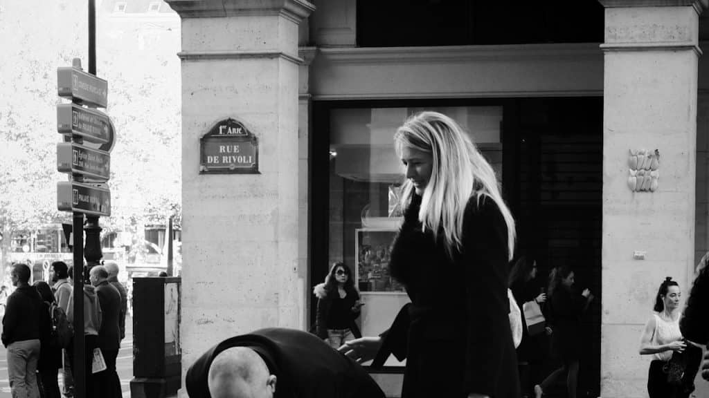 A woman touching the back of a man who’s bent over in pain while they stand on a street.