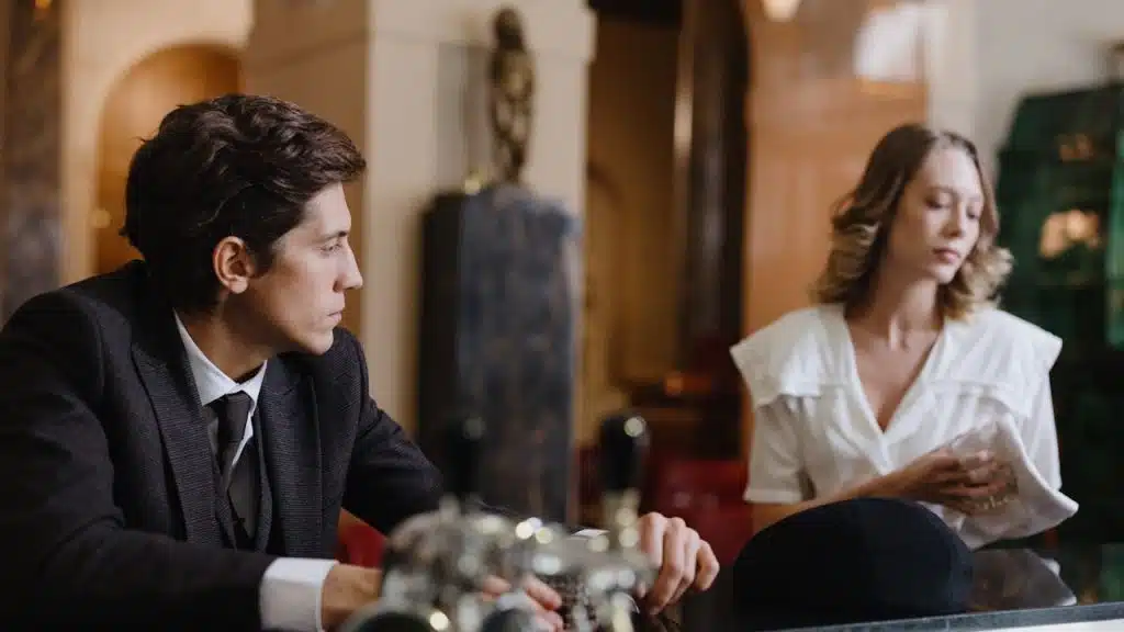 Man in a suit looking away from a woman at a bar counter.