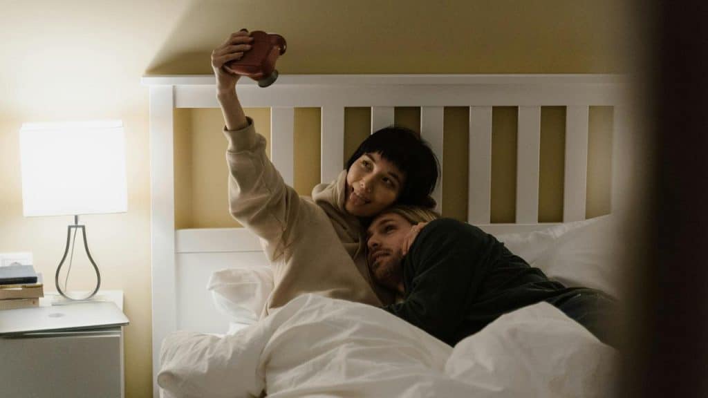 A couple lying in bed, taking a playful selfie together.
