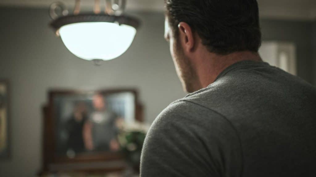 Over-the-shoulder view of a man in a gray shirt looking at a mirrored reflection.