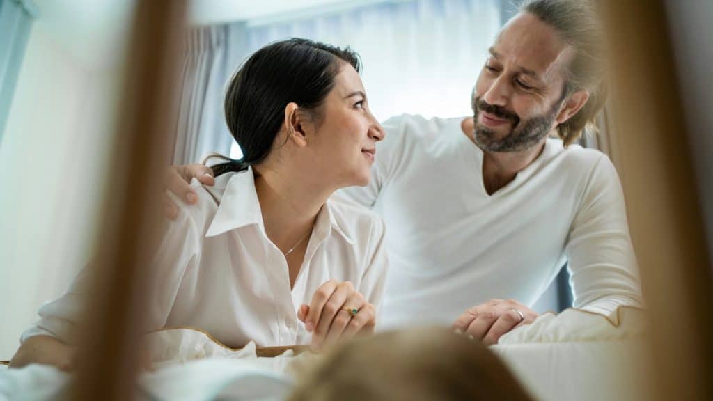 Smiling couple looking lovingly at each other over a baby crib.