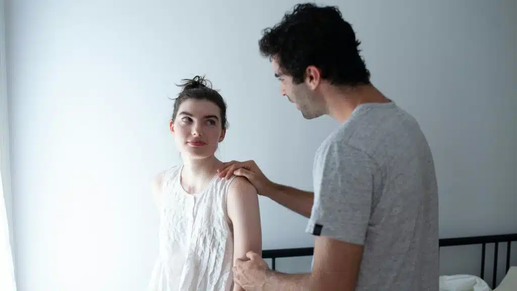 A man holding a woman’s shoulder and arm in a bedroom.