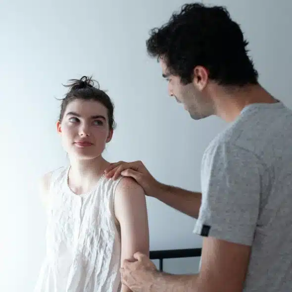 A man holding a woman’s shoulder and arm in a bedroom.