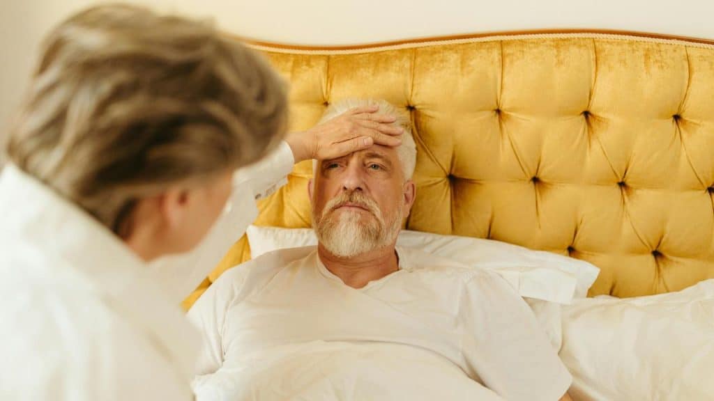 A woman checking a man’s forehead as he lies in bed.