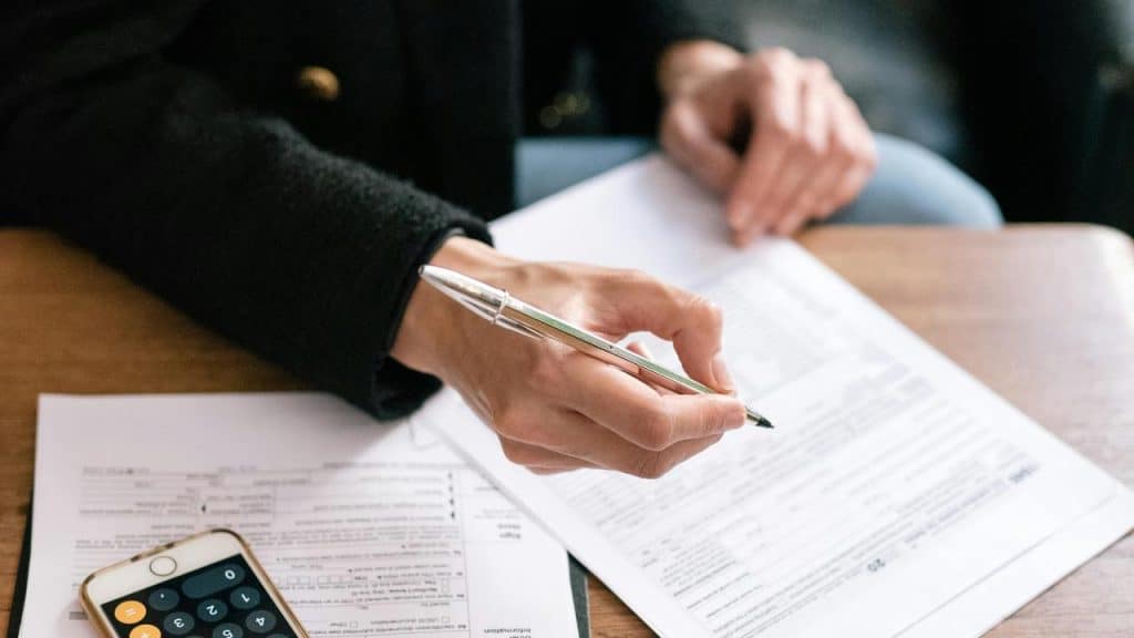 A person reviewing and filling out paperwork with a pen and phone nearby.