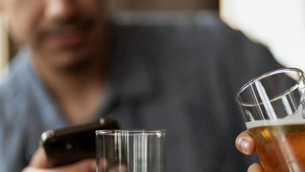 A person holding a beer glass while looking at a phone.
