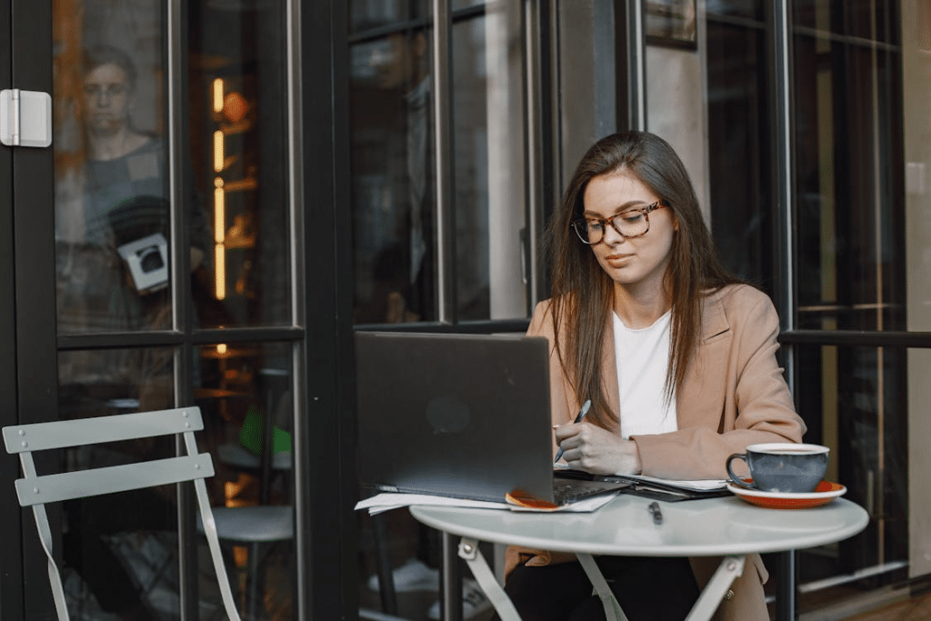 Woman Wearing Eyeglasses Sitting in the Coffee Shop Using Her Laptop and Taking Notes