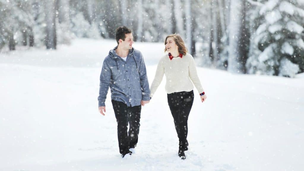 A man and a woman holding hands while walking in snowfall.