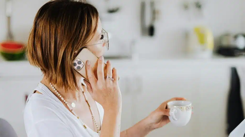 A woman talks on the phone while holding a cup in her other hand.
