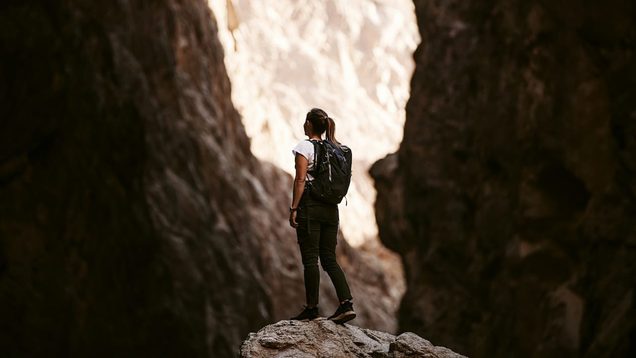 A woman with a backpack standing on a rock between two cliffs. 