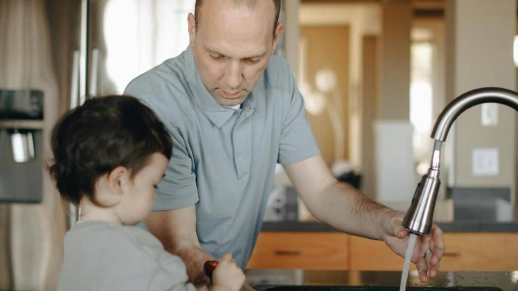 A man helping a child wash something at a kitchen sink.