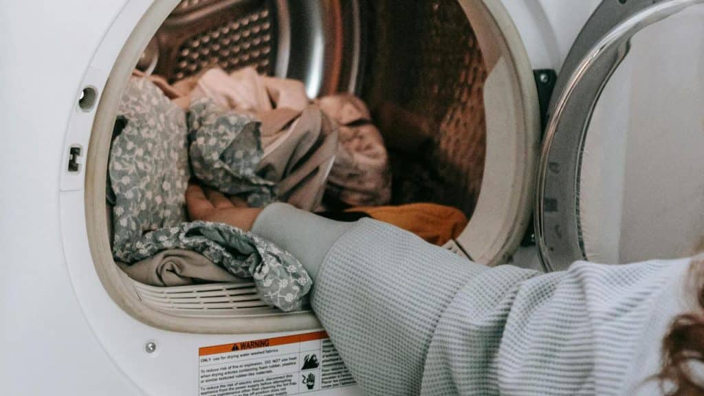A person reaching into a dryer to remove a load of laundry.