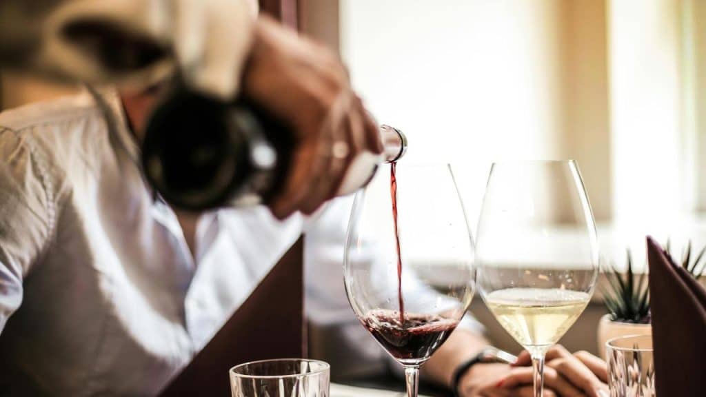 A person pouring red wine into a glass at a restaurant table.