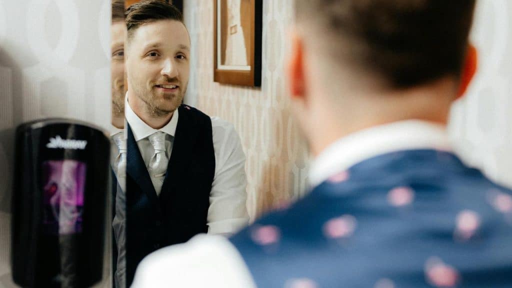 A man in a suit smiling at his reflection in a mirror.