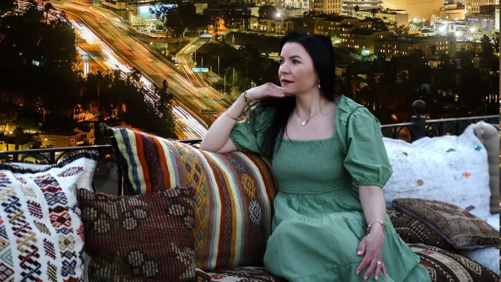 A woman is standing on a rooftop with a view of city in the background.