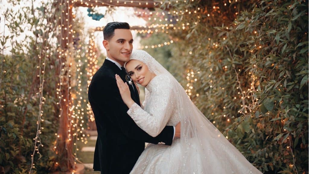 Bride and groom embracing with festive lights in the background.