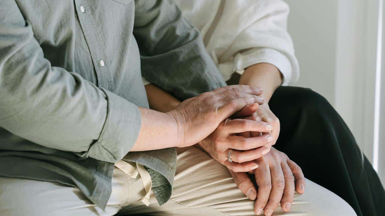 A close-up of two people sitting with their hands gently resting together.