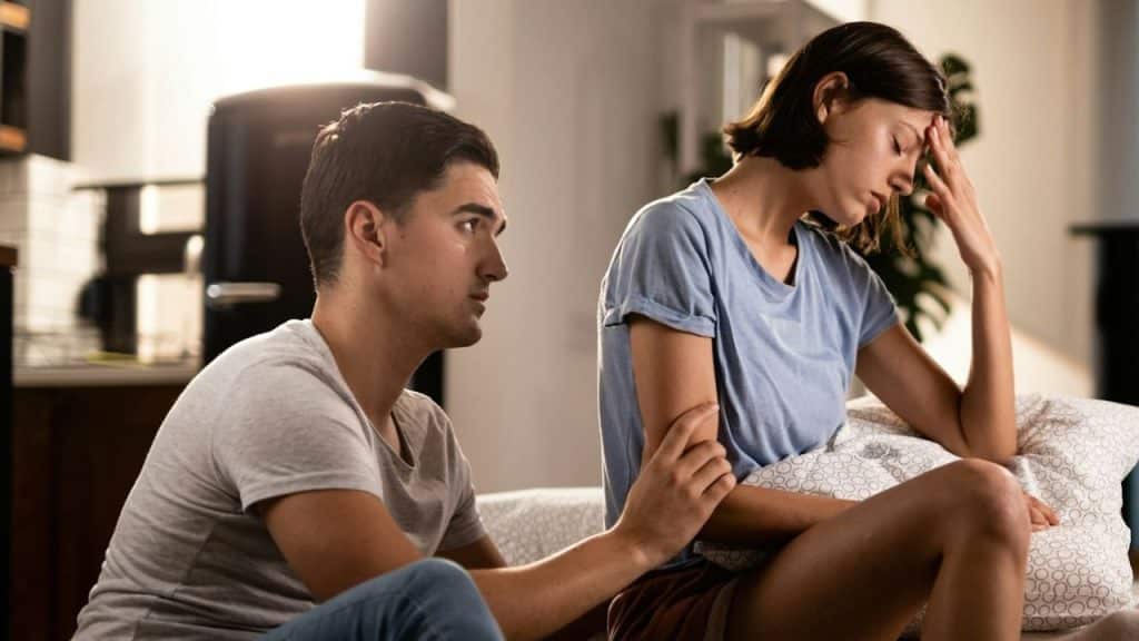 Man comforting a distressed woman who is holding her head with her hand.