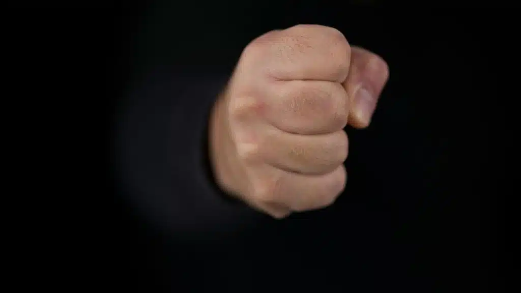 A clenched human fist emerges from a dark, black background.