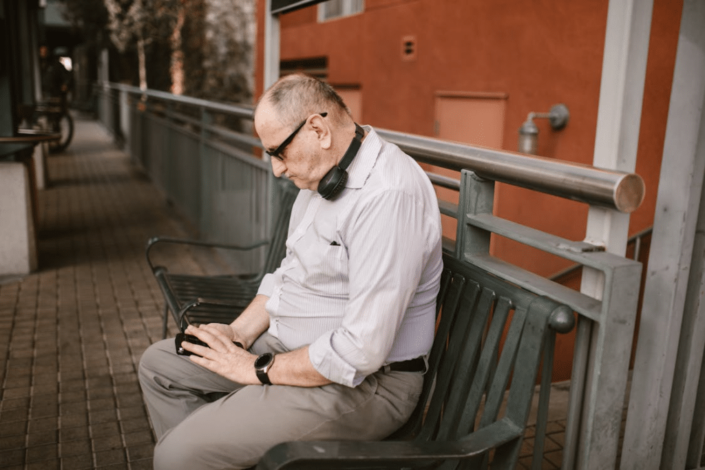 Elderly Man in White Long Sleeves Sitting on Metal Fence