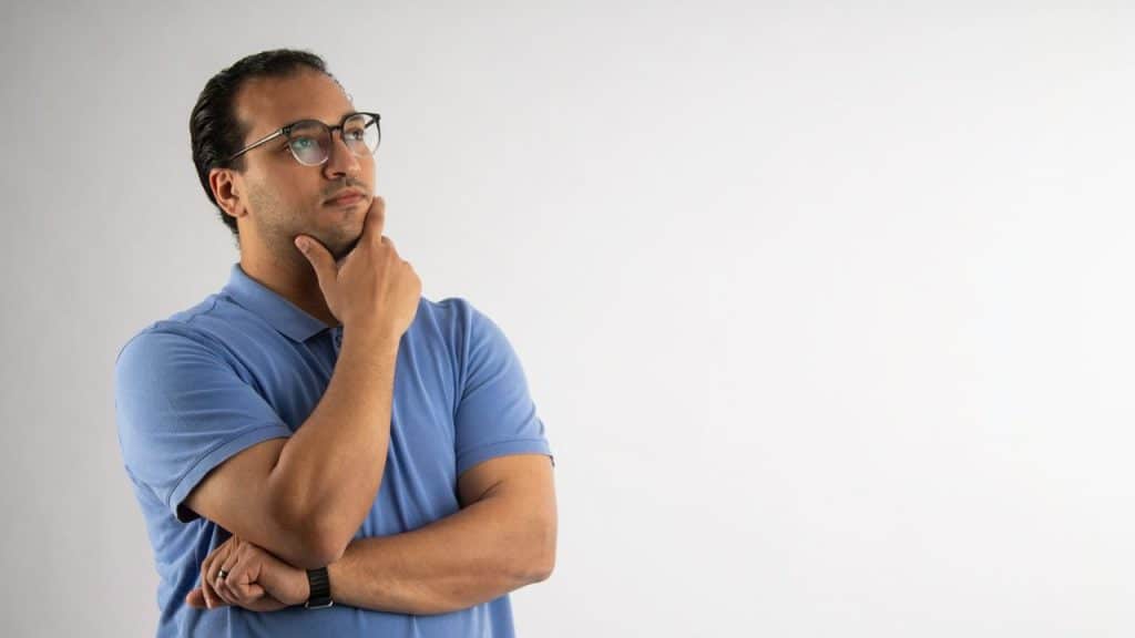 Man in a blue polo shirt standing with his hand on his chin, thinking.