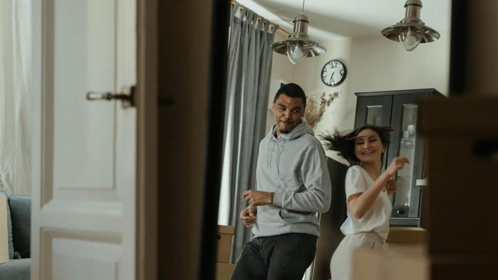 A happy couple dances playfully together in their living room.