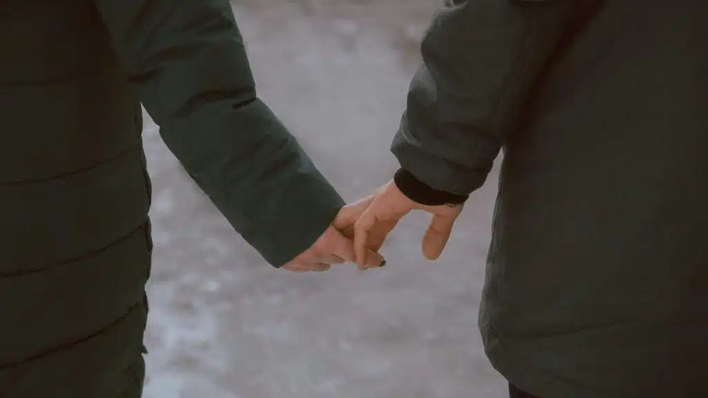 A couple holding hands while walking outdoors in winter coats.