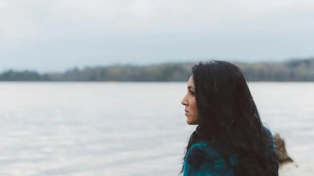 A woman looks out over a calm lake on a cloudy day.