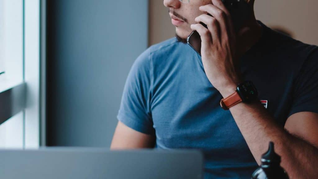 A man talking on the phone while sitting near a laptop.