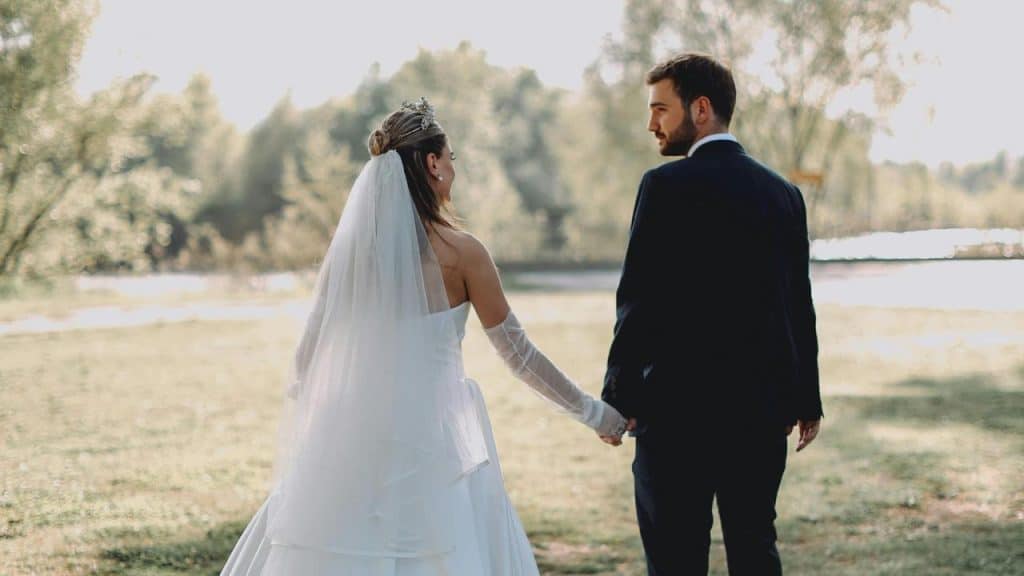 A bride and groom hold hands while walking outdoors.