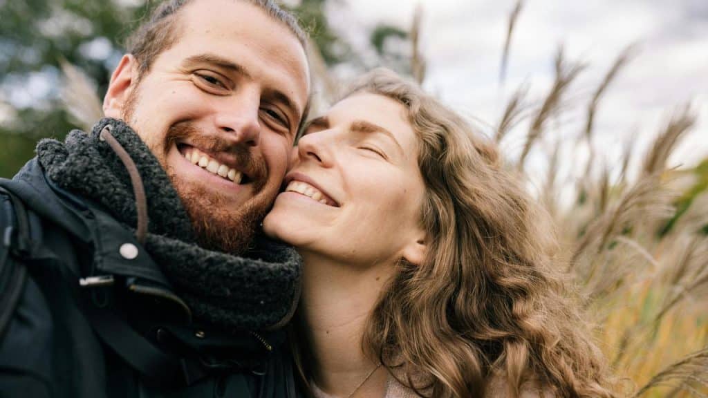A smiling couple taking a close-up selfie outdoors.