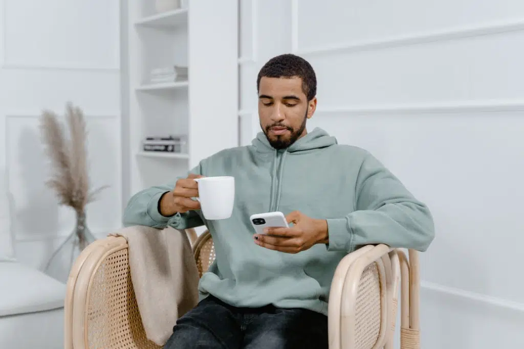 Man in a Hoodie Sitting on an Armchair Holding White Ceramic Mug