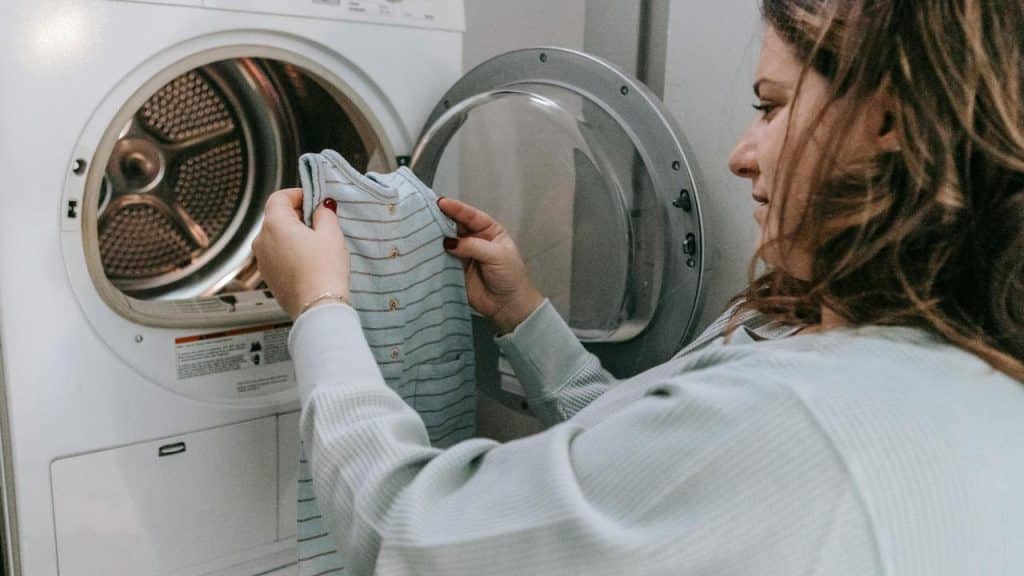 A person loading a striped baby outfit into a washing machine.