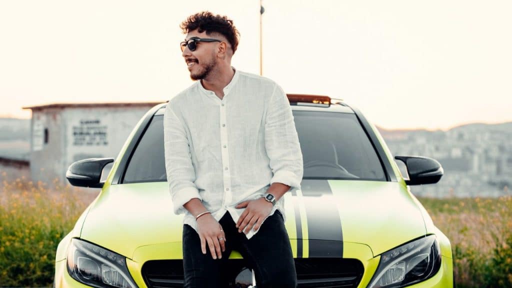Smiling man leaning against the hood of a bright yellow sports car outdoors.