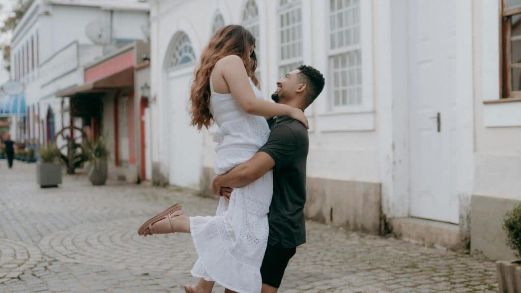 A man lifting a woman in a white dress as they smile together.