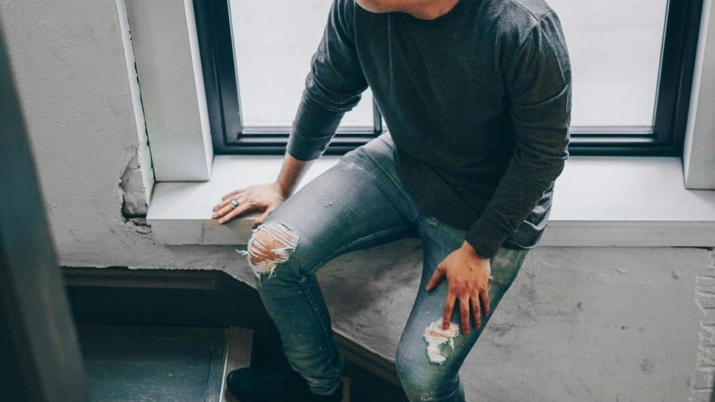 A person sitting on a windowsill wearing a dark shirt.