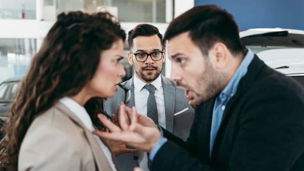 Two people arguing in the foreground, with a man watching them in the background.