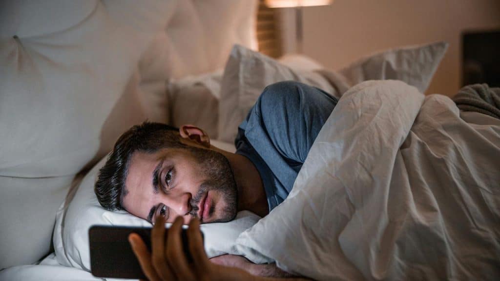 A man lying in bed looking at his phone.