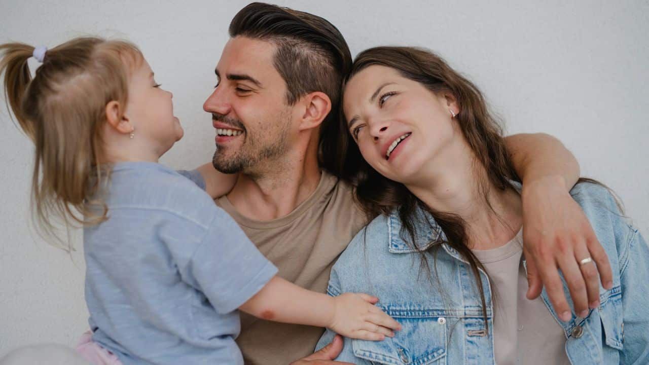 Smiling family close-up: man hugging woman in denim, girl touching the man's face.