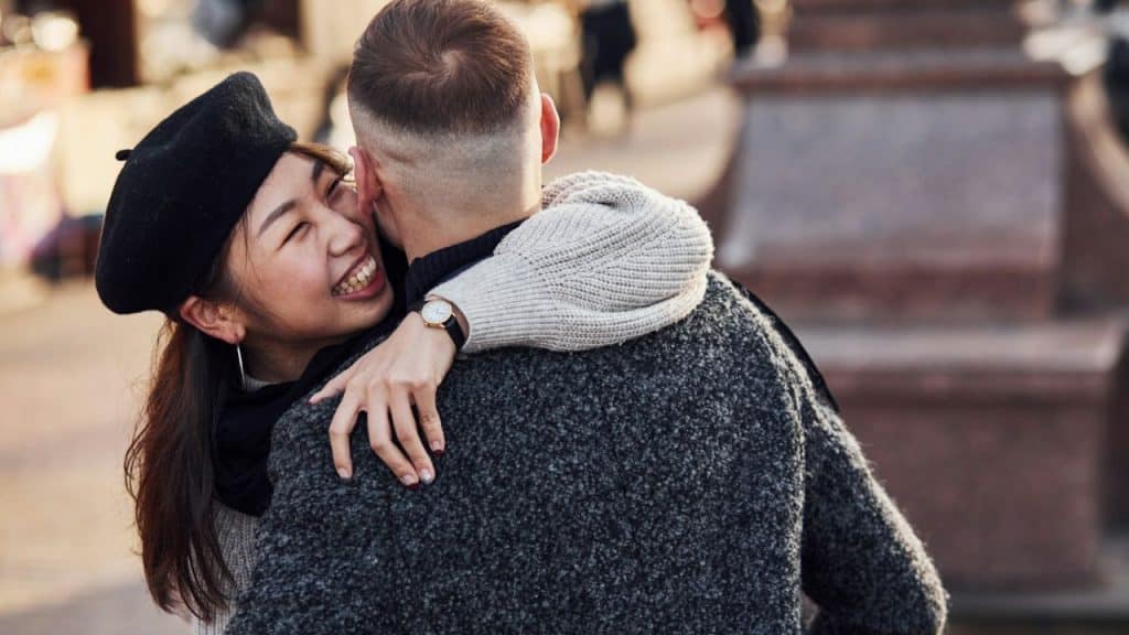 Young woman in a black beret embracing a man from behind, laughing happily.