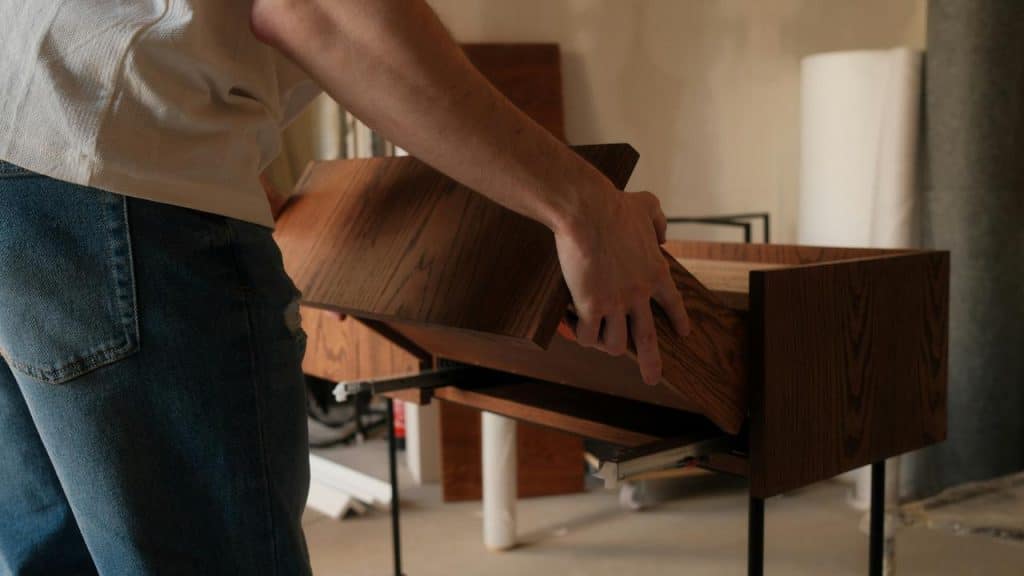 A person assembles a wooden drawer, holding a panel while working in a workshop.