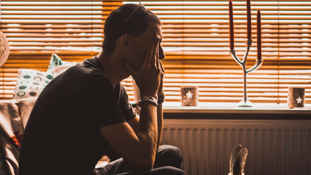 A man with sunglasses on his head hiding his face with his hands and appearing distressed.
