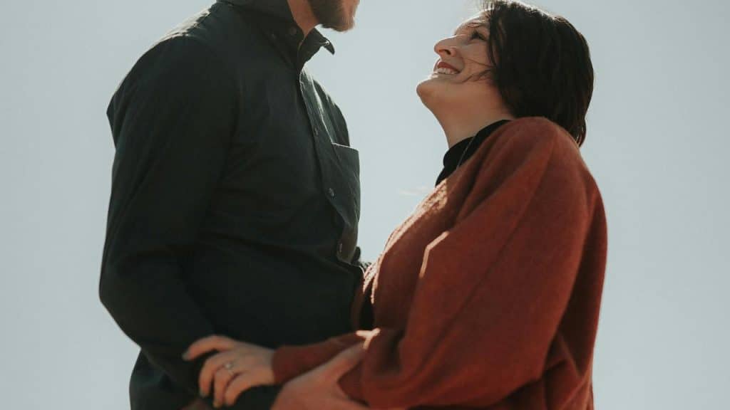 A couple smiles warmly at each other while holding hands outdoors.