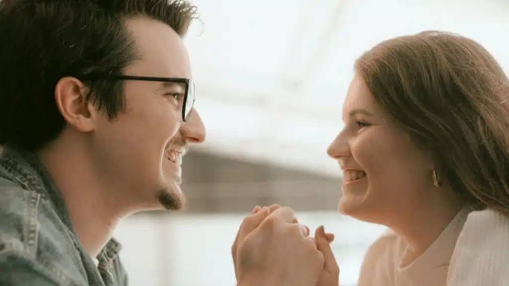 A man in glasses and a woman smiling at each other while holding hands.