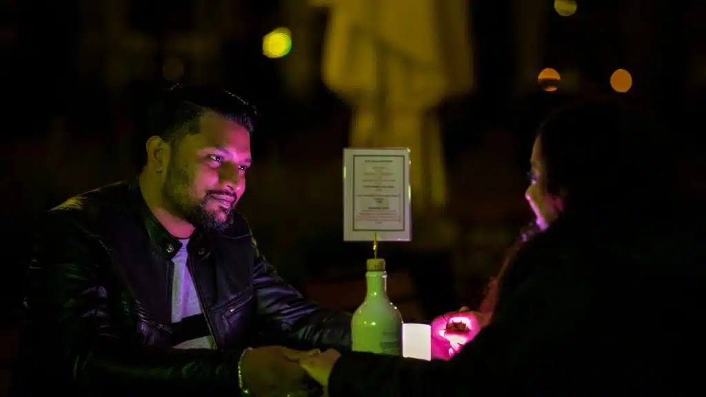 Couple holding hands across a table in a dark, outdoor restaurant setting.