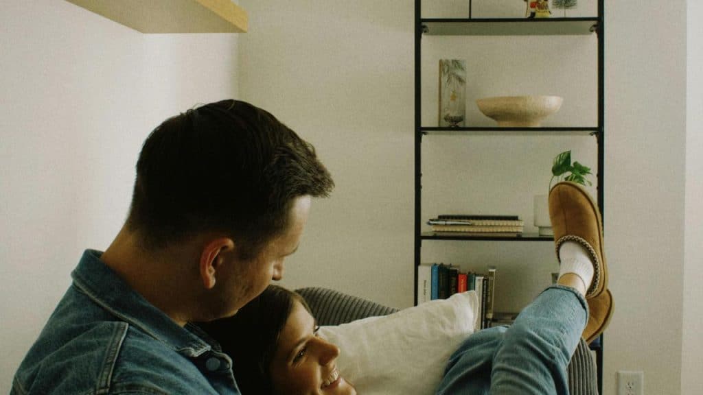 A couple relaxing together indoors, smiling while sitting on a couch.